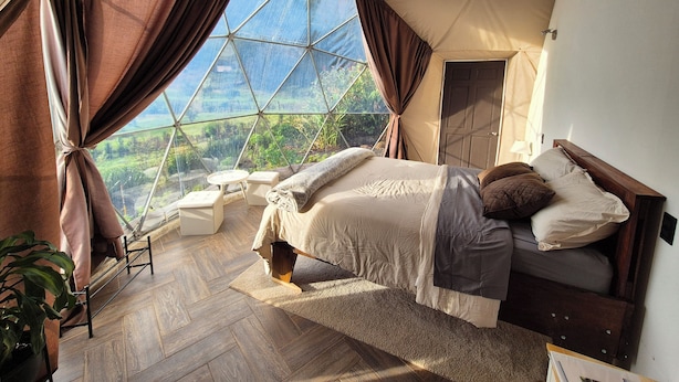 A bedroom with a large window, a bed, a bedside table, and a chair. - Glampling Nubes de Monteverde (Monteverde)