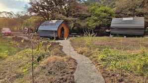 Two cylindrical cabins with wooden doors and a gravel path leading to them, surrounded by greenery and hills. - Glampling Nubes de Monteverde (Monteverde)
