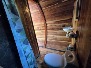 A compact bathroom with a wooden floor, a white sink, and a toilet. - Glampling Nubes de Monteverde (Monteverde)