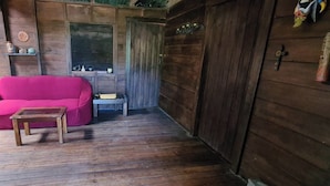 A wooden interior with a pink sofa and a small table, wooden flooring, and a door with a window. - Glampling Nubes de Monteverde (Monteverde)