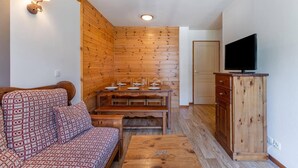 Ett mysigt rum med en soffa, ett matbord i trä, en tv-apparat placerad på ett träskåp och en väggpanel i trä.