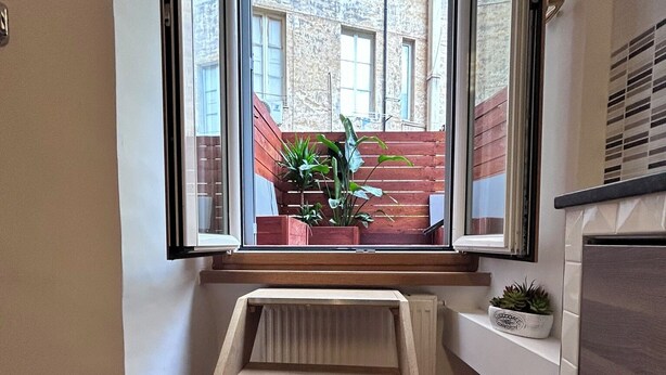 A small, narrow room with a window overlooking a brick building. There is a wooden bench at the window and a small shelf with a plant. - Maison Vaticana (Rome)