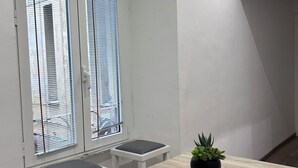 A small, modern room with a wooden table and two white bar stools. There is a window with blinds, and a potted plant on the table. - Maison Vaticana (Rome)