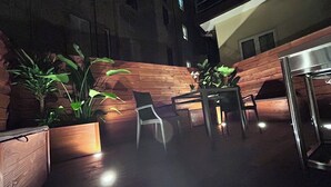 An outdoor patio area with wooden flooring, potted plants, a table with chairs, and a metal table. - Maison Vaticana (Rome)
