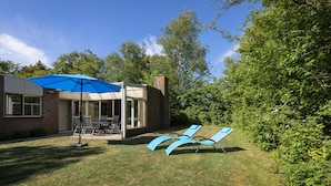 A backyard with a patio, outdoor furniture, and a blue umbrella. - Bungalow in North Holland Near the North Sea (Sint Maartensvlotbrug)