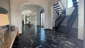 Ein geräumiger Flur mit schwarzem Marmorboden, einer Treppe mit schwarzen Geländern und einem Essbereich im Hintergrund.