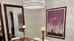 Ein Essbereich mit einem Holztisch, weißen Stühlen, einer Kristallleuchtre und gerahmten Kunstwerken an der Wand.