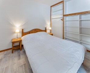 A neatly made bed with a wooden headboard, two bedside tables with lamps, and a built-in shelving unit against the wall. - Resort center, 2nd floor, fitness, swimming pool, sauna, balcony, tv, ski locker, 40m², Les Orres (Les Orres)