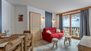 Ein gemütliches Zimmer mit einem Holzespeisetisch, einem roten Sofa und einem Balkon mit Blick auf eine verschneite Landschaft.
