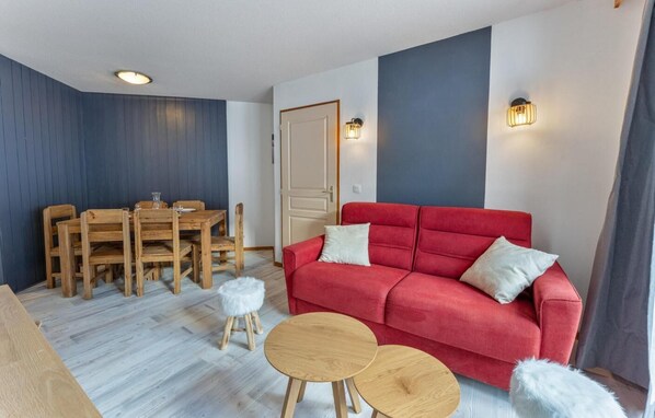 A room with a red sofa, wooden dining table, and chairs. There are two small round tables and a white fluffy stool. - Resort center, 2nd floor, fitness, swimming pool, sauna, balcony, tv, ski locker, 40m², Les Orres (Les Orres)