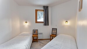 Ein Zimmer mit zwei Einzelbetten, einem Fenster mit Blick auf Bäume und Wandleuchten.