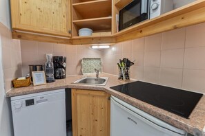 A compact kitchen with wooden cabinets, a built-in microwave, a sink, and a dishwasher.