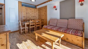 A cozy room with a wooden dining table, chairs, a sofa with patterned cushions, and two wall-mounted lamps. - 40m from ski slopes, 1st floor, fitness, swimming pool, sauna, balcony, tv, ski locker, 40m² (Les Orres)