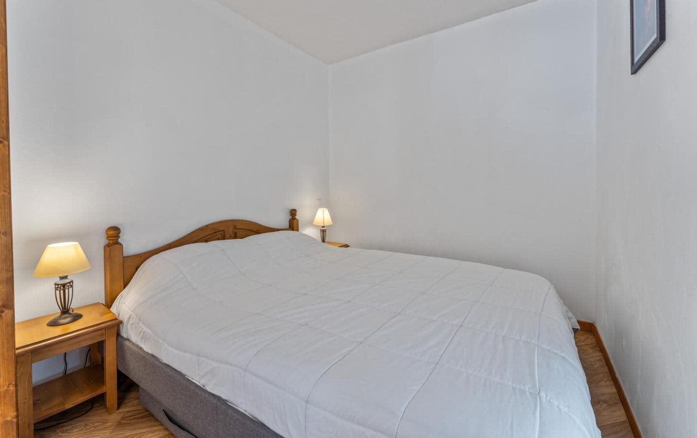 A single bed with a wooden headboard, two bedside tables with lamps, and a plain white wall.