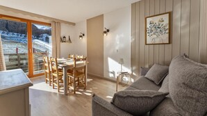 Uma sala de estar moderna com uma mesa de jantar de madeira, sofá cinza e uma grande janela com vista para uma paisagem nevada.