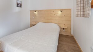 Quarto com cabeceira de madeira, cama com edredom branco e uma pequena mesa de cabeceira.