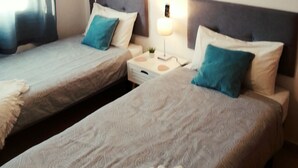 A hotel room with two single beds, a nightstand with a lamp, an air conditioning unit, and a painting on the wall. - LUNA HOUSE 😎 (Santiago de la Ribera)