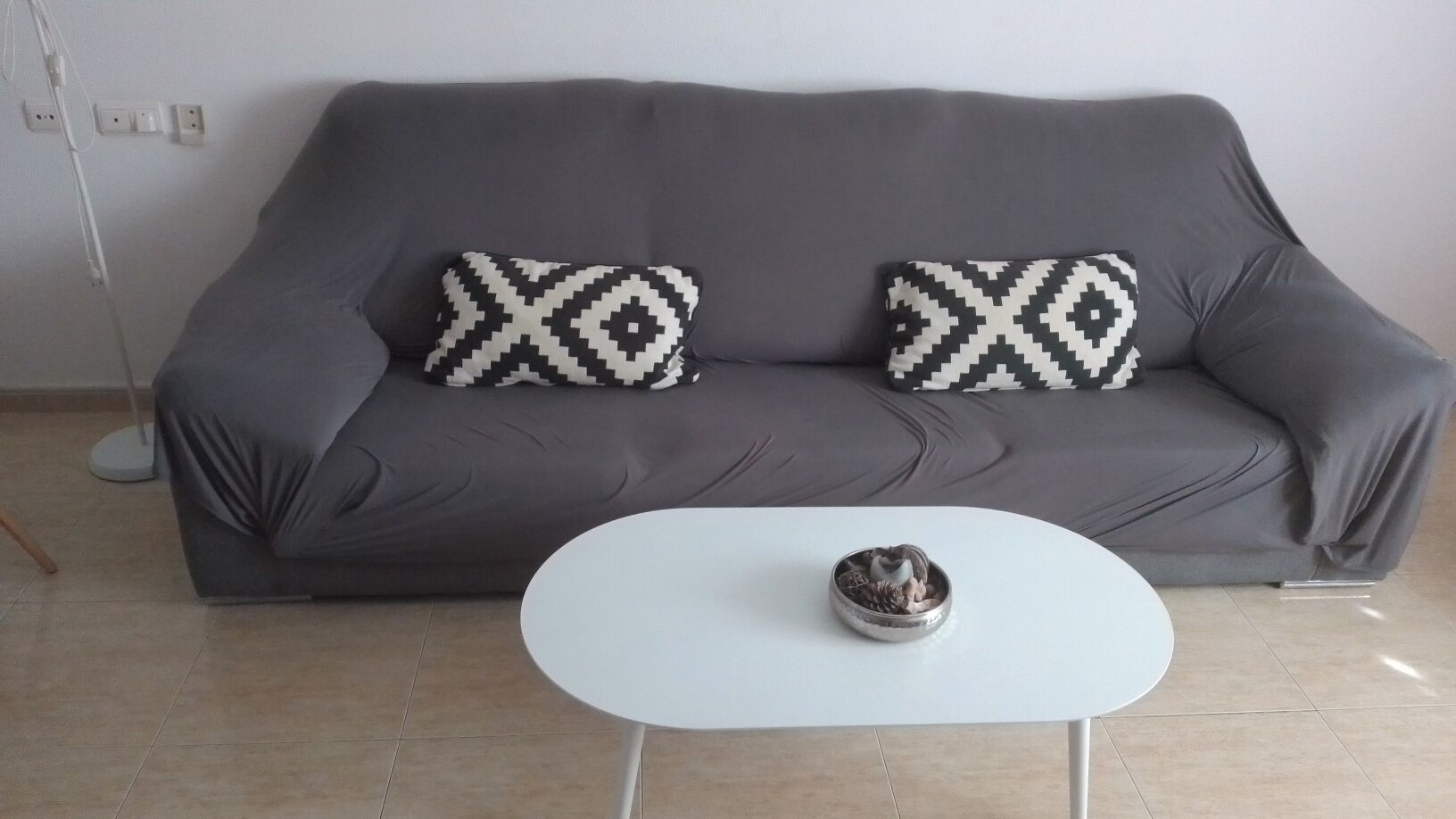 A grey sofa with patterned cushions, a white coffee table, and a small decorative bowl.