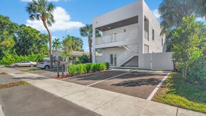 A modern two-story building with a white exterior, a covered parking area, and surrounding greenery including palm trees. - Modern 3BR Near Beaches–Fast WiFi & Spacious Design (Fort Lauderdale)