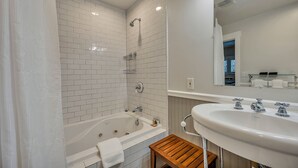 Een moderne badkamer met een witte betegelde douche, een badkuip, een houten krukje en een groot wastafelmeubel met een spiegel erboven.