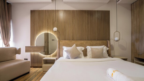Hotellihuone, jossa on suuri sänky, sohva, yöpöytä, peili ja puinen seinäpaneeli.