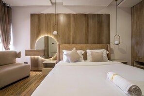 A hotel room with a large bed, a sofa, a bedside table, a mirror, and a wooden wall panel. - George Residence Nike Art Gallery Rd  (Lekki)