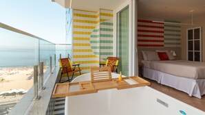 Un balcón con vistas a la playa, una cama con cubrecama blanco y una pared con un colorido diseño de azulejos.