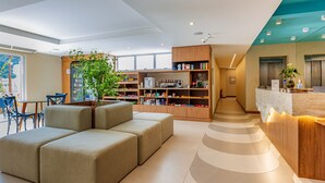 A modern hotel lobby with a seating area, a reception desk, and a large bookshelf.