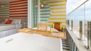A modern hotel room with a bed, a wooden side table, and a view of the beach.