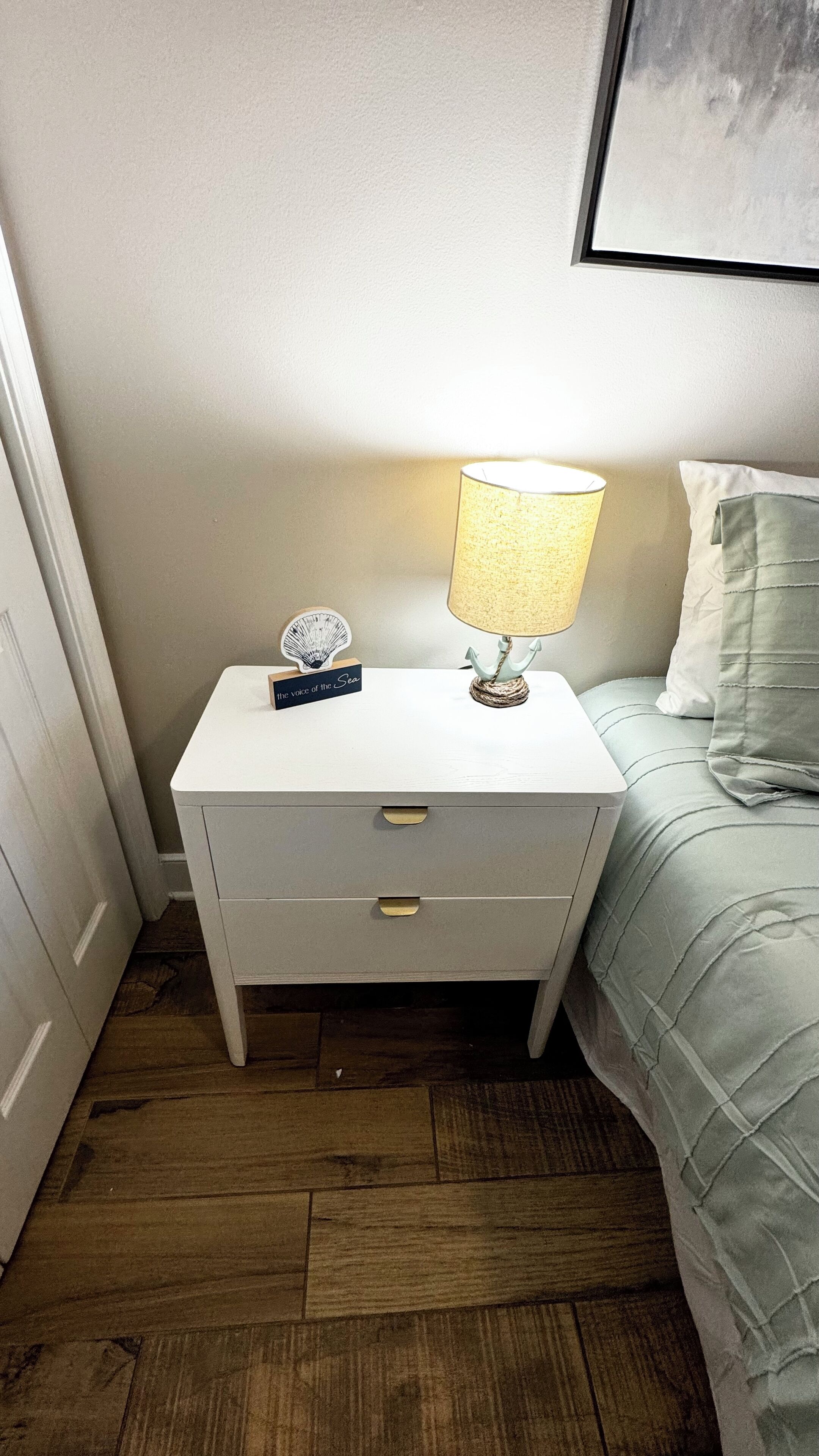 A white bedside table with a lamp, a small decorative item, and a drawer.