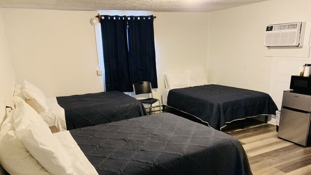 A room with two beds, a chair, a desk, and an air conditioning unit.