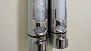 Two cylindrical objects with reflective surfaces and a central void, mounted on a plain wall.