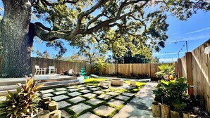 A backyard with a wooden deck, a stone pathway, and a large tree providing shade.