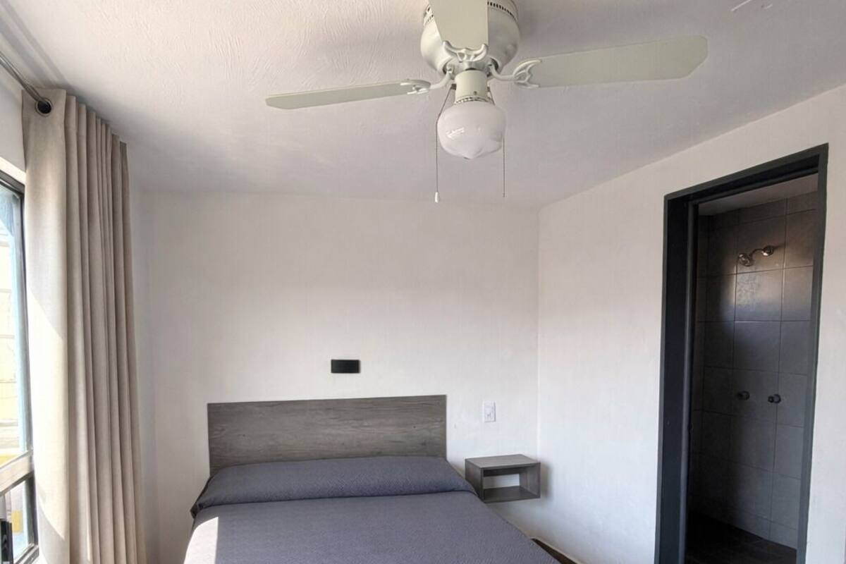 Una habitación de hotel moderna con cama, ventilador de techo y una puerta que da a un baño.
