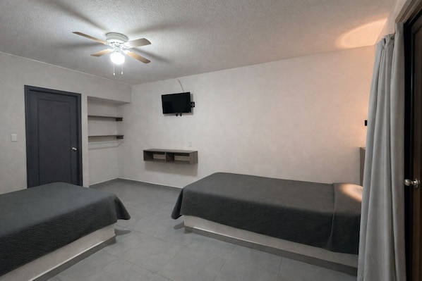 Une chambre avec deux lits simples, un ventilateur de plafond, une télévision et une porte.