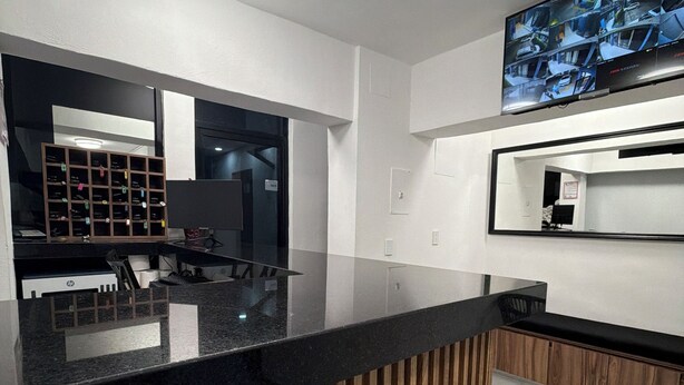 Una cocina moderna con encimera negra, paneles de madera y un televisor de pantalla plana grande montado en la pared.