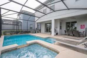 Una piscina con jacuzzi, mobiliario exterior y un patio cubierto.