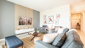 Ein modernes Wohnzimmer mit einem grauen Sofa, einem blauen Ottomanen und einer gestreiften Wandverkleidung.