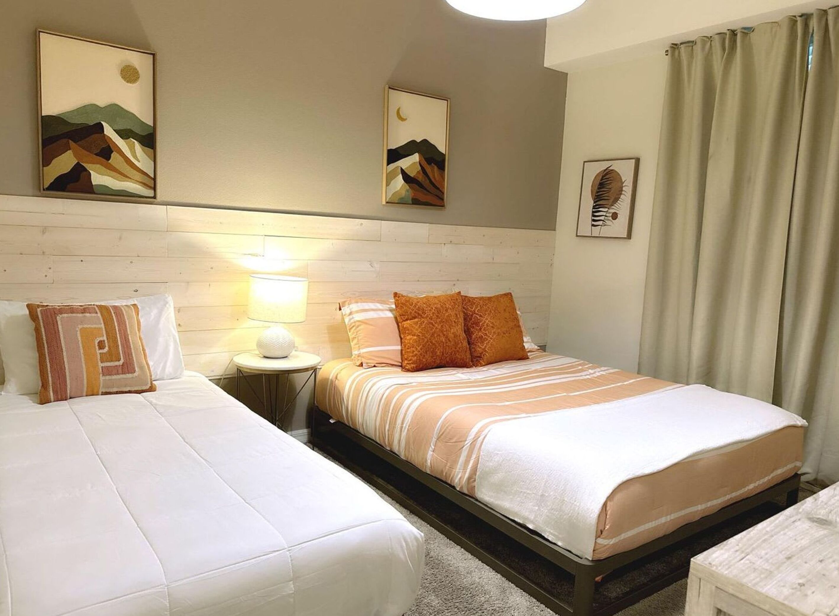 A bedroom with two beds, a nightstand with a lamp, and artwork on the walls.