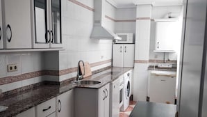 Una cocina compacta con armarios blancos, encimera de granito, microondas integrado y lavadora.