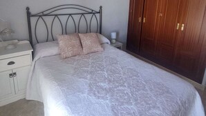 Una cama bien hecha con una colcha estampada, una mesita de noche con una lámpara y un armario con espejo.