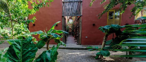 A courtyard with a red wall, a wooden gate, and lush green plants.