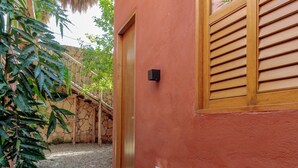 Un sentier pavé de pierres mène à un bâtiment à l’extérieur rouge, doté d’une porte en bois et d’une fenêtre avec des volets en bois.