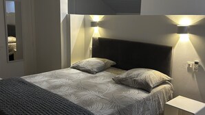 Une chambre moderne avec un grand lit, deux lampes fixées au mur, une table de chevet et une porte donnant sur une autre pièce.
