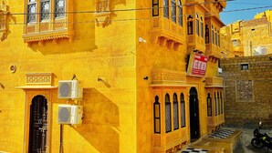 A yellow building with intricate architectural details, a checkered entrance, and a sign indicating it is a hotel.