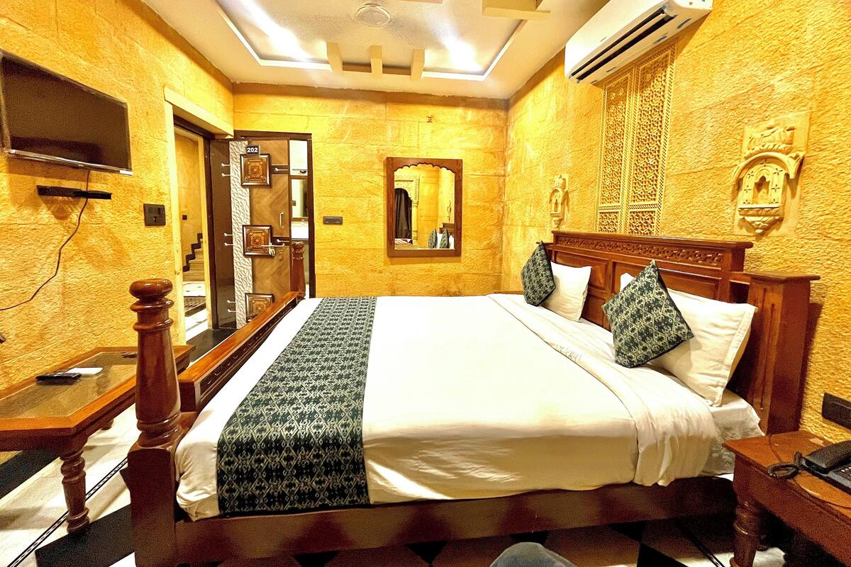 A hotel room with a large bed, a wooden headboard, a flat-screen TV mounted on the wall, and a ceiling fan.