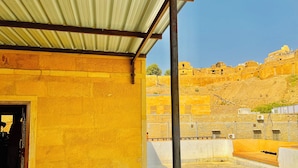 A building with a yellow exterior, a metal roof, and a view of a hill with ancient structures.