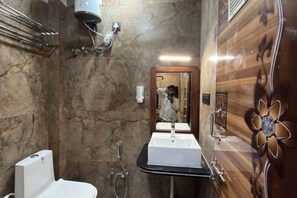 Un baño con pared de mármol, lavamanos blanco, espejo y ducha.