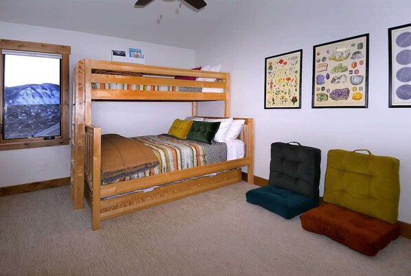 Una cama individual con vista a un paisaje montañoso, un ventilador de techo e impresiones botánicas enmarcadas en la pared.
