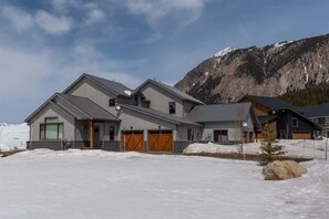 A modern two-story house with a garage, large windows, and a view of a mountain.